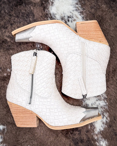 White woven ankle boots with beige soles on a textured brown surface