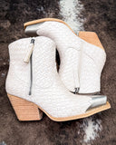 White woven ankle boots with wooden block heels on a textured surface