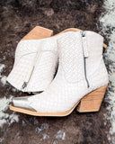 White woven ankle boots with wooden block heels on a textured brown surface
