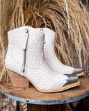 White woven ankle boots with wooden heel on a round wooden platform against a natural background.