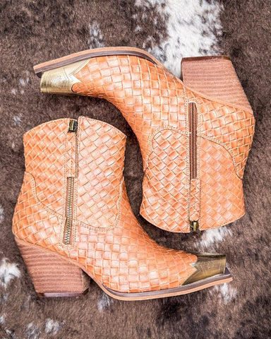 Pair of woven tan ankle boots with gold accents on a textured surface