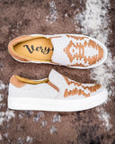 Pair of white sneakers with brown accents on a textured brown surface
