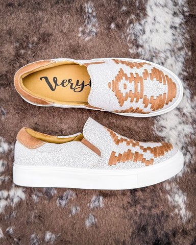 Pair of white sneakers with brown accents on a textured brown surface
