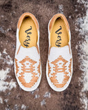 Pair of white slip-on shoes with brown patterns on a textured brown surface