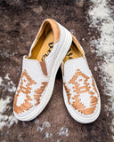 White slip-on sneakers with brown patterned sole on a textured surface