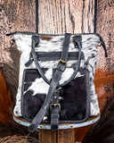 Black and white cowhide leather bag with straps on a wooden background