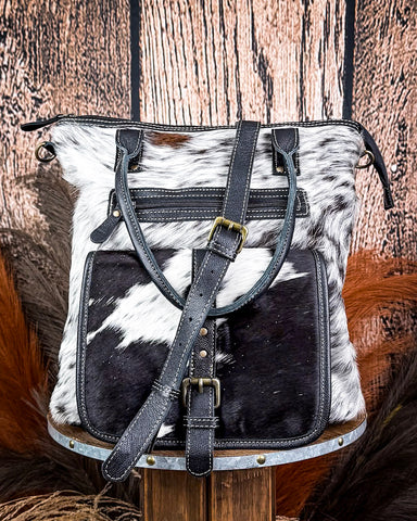 Black and white cowhide leather bag with straps on a wooden background