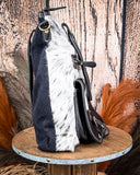 Black and white cowhide leather bag on a wooden stand with a rustic background