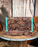 Brown leather handbag with turquoise accents on a wooden surface