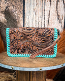 Handbag with turquoise edge and intricate brown leather design on a wooden surface.