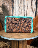 Turquoise and brown leather wallet with intricate designs on a wooden surface.