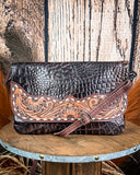 The Duskline Embossed Crossbody Purse displayed on a wooden table with wheat behind it, sitting in front of a wood back drop.