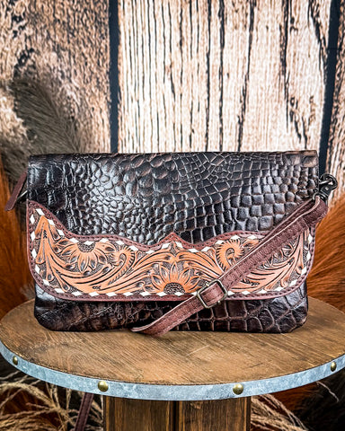 The Duskline Embossed Crossbody Purse displayed on a wooden table with wheat behind it, sitting in front of a wood back drop.