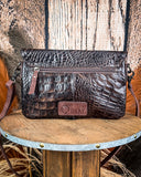 Back view of the Duskline Embossed Crossbody Purse displayed on a wooden table with wheat behind it, sitting in front of a wood back drop.