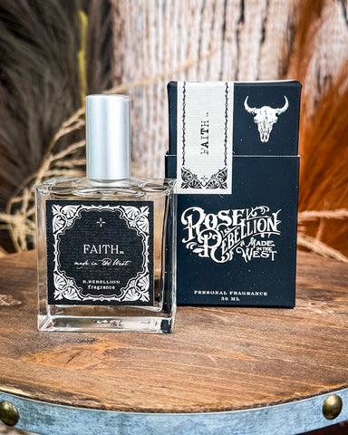Perfume bottle and packaging with 'Faith' and 'Rose Rebellion' branding on a wooden surface.