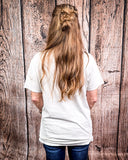 Person wearing a white t-shirt and blue jeans, standing against a wooden background.