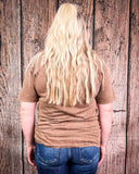 Person wearing a brown t-shirt and blue jeans standing against a wooden wall.