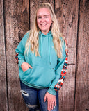 Person wearing a teal hoodie with colorful sleeves against a wooden background