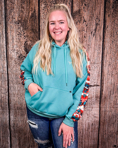 Person wearing a teal hoodie with colorful sleeves against a wooden background