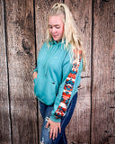 Person wearing a teal hoodie with colorful sleeves against a wooden background