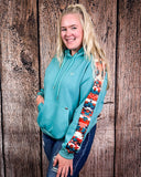 Person wearing a teal hoodie with colorful sleeves against a wooden background