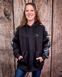 Person wearing a black hoodie with colorful sleeves against a wooden background