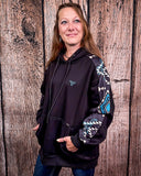 Person wearing a black hoodie with a patterned sleeve against a wooden background