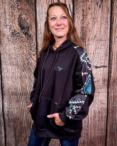 Person wearing a black hoodie with a patterned sleeve against a wooden background