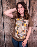 Woman wearing a graphic t-shirt with a design of a bronc and boots against a wooden background