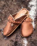 Pair of brown mule sandals with braided detail on a textured surface
