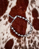 Silver beaded bracelet on a brown and white patterned fabric background