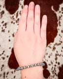 Hand wearing a silver bracelet on a patterned background