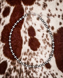 Silver beaded necklace on a brown and white patterned fabric background
