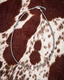 Necklace with pink conch on a brown and white patterned fabric background