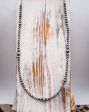 Silver beaded necklace on a wooden surface with a white background