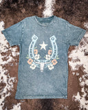 Grey t-shirt with horseshoe and star design on a brown and white patterned surface