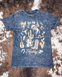 Black t-shirt with western-themed graphics on a textured brown background