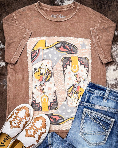 Brown t-shirt with graphic design, blue jeans, and white shoes on a textured surface