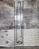 Necklace with a pendant on a wooden surface next to a ruler for measurement.