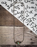 Necklace with a turquoise pendant on a wooden surface with a white paper background featuring black text.