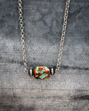Necklace with a large turquoise bead and smaller silver beads on a textured gray background