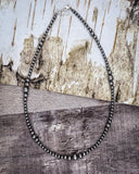 Silver beaded necklace on a wooden surface with a rustic background