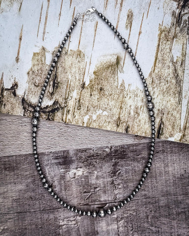 Silver beaded necklace on a wooden surface with a rustic background