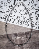 Silver beaded necklace on a wooden surface with abstract black and white patterns in the background