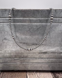 Silver beaded necklace on a textured tin surface