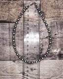 Silver beaded necklace on a wooden surface with a ruler for scale