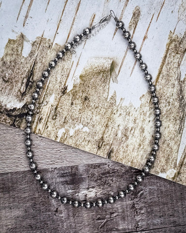 Silver beaded necklace on a wooden surface with a textured background