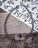 Silver beaded necklace on a wooden surface with a white paper background featuring black text.