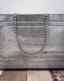 Silver beaded necklace on a textured gray surface