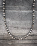 Silver beaded necklace on a textured gray background